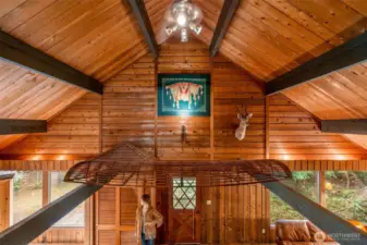 From the balcony, the lodge shows off its quirks—native artwork glowing in the spotlight, stretched across a high window like a tapestry. Just below, the canoe rests in quiet retirement, while the deer keeps its post. And below? Madeline stands ever-watchful, making sure you don’t miss a thing.