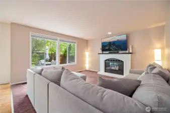 Cozy family room features a white brick fireplace with mantle, large windows, and backyard views—perfect for relaxing or movie nights.