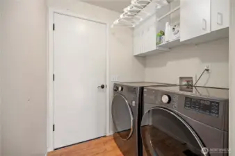 Functional laundry room with front-load washer/dryer, upper cabinets for storage, and hanging rack.