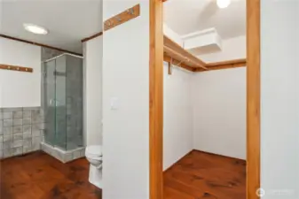The primary ensuite bathroom, showing the shower, toilet, and walk-in closet. The flooring is wide plank, real wood floors with cut nails. The flooring on the main level needs refinishing, home is priced accordingly.