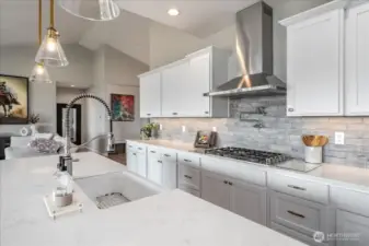 View of kitchen with quartz countertops, stainless appliances, tile backsplash and pot filler.