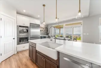 View of kitchen with quartz countertops, pendant lights, farmhouse sink and stainless steel appliances.