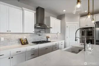 View of kitchen with quartz countertops, pendant lighting, stainless steel appliances and tile backsplash.