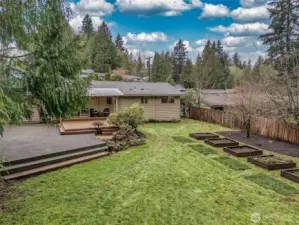 Spacious backyard with a large deck, open lawn, and raised garden beds.