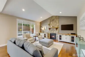 Open concept living space with vaulted ceilings, gas fireplace, and stone accent wall with mantel.