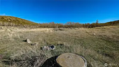 A comprehensive view looking SE from the NW corner of the property. This angle highlights the varied terrain and includes a unique historical feature—a dry, hand-dug well site. A great reference point for those looking to explore the full 360-degree potential of this acreage. This would make a great camping area.