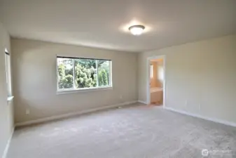 This view of the primary suite shows the entry to the private bathroom and large picture window for plenty of natural lighting.