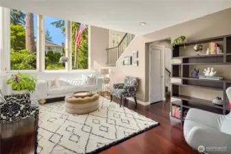 Bathed in natural light, this stunning living room features soaring double-height ceilings and expansive picture windows framing lush greenery. Elegant design details include a tufted sofa, statement lighting, and a graceful staircase—creating a warm, welcoming first impression....