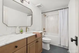 Lower-level full guest bathroom with deep soaking tub, custom tile surround, slate tile flooring, vanity with soft close drawers/doors, marble countertop, shiplap wall detail and high-end plumbing fixtures.