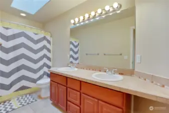 Upstairs full bathroom with double vanity sinks and skylight.