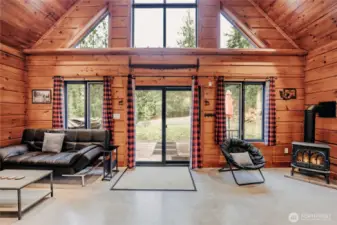 Living room anchored by architectural windows, vaulted ceilings & rustic pine log walls