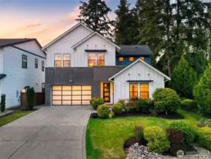 This stunning modern farmhouse blends crisp architectural lines with warm, inviting interiors, all set against a backdrop of lush evergreens. Featuring a striking brick and board-and-batten exterior, manicured landscaping, and a glowing welcome through oversized windows and a contemporary glass-panel garage.