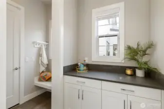 This stylish and functional drop zone connects the garage to the kitchen, offering built-in cabinetry, counter space, and a cozy bench with hooks for effortless organization. It's the perfect landing spot for bags, coats, and daily essentials—keeping clutter out of sight and convenience within reach.