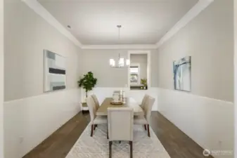 This elegant formal dining room features crisp wainscoting, warm hardwood floors, and a modern light fixture, creating a refined space for entertaining. A convenient pass-through leads to the drop zone, adding both function and flow to this thoughtfully designed layout.