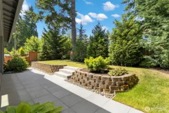 The backyard is a private, sun-dappled oasis bordered by mature evergreens and thoughtfully landscaped with tiered garden beds and stone retaining walls. With a spacious patio and lush lawn, it’s perfect for relaxing, entertaining, or simply enjoying the serenity of nature.