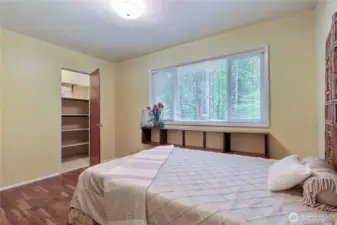 This bedroom features hardwood floors, a storage closet, and large windows looking out to the wooded landscape.