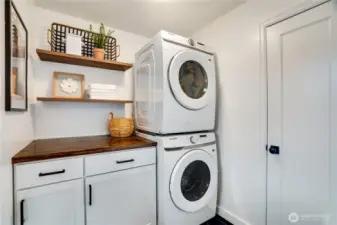 Convenient dedicated laundry room with brand-new Samsung front-load washer and dryer (stacked), custom folding counter with butcher-block top, shaker cabinets for storage, open shelving, and stylish finishing touches. Clean, bright, and perfectly organized.