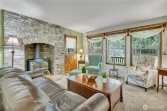 Bright living area with wood-trimmed windows and a substantial brick alcove for the woodstove, perfect for warmth and comfort.