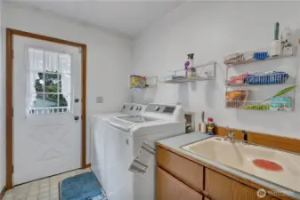 Well-appointed utility room featuring a sink, ample lower cabinets, and a door providing direct access to the back deck.