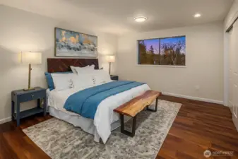 Your primary retreat awaits. This generous bedroom offers warm wood tones, a large picture window with sunset views, and ample space for a king-sized suite.