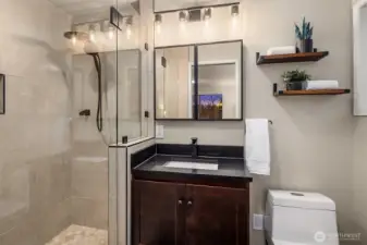 Spa-inspired luxury. The renovated bathroom features a sleek black quartz vanity, modern industrial lighting, and a stunning glass-enclosed walk-in shower