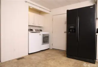 The laundry area features newer washer and dryer units that stay with the property, offering convenience and reliability. It’s easy to add a door or curtains to neatly conceal the space if desired. The door shown provides direct access to the backyard, and one of the two refrigerators is also visible in this view.