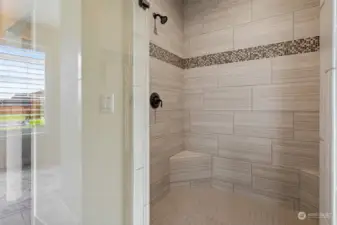 Custom tiled walk-in shower with inlay, glass door, and two shower heads.