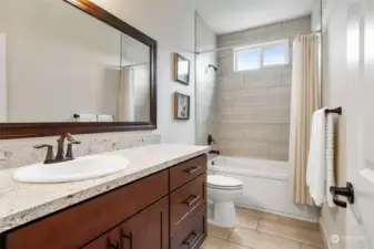 Guest bathroom offers tile flooring and surround in shower/tub. Granite counter on sizable vanity with cabinet and drawer storage.