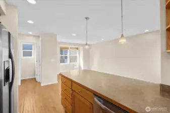 Kitchen island with pendant lighting, wood flooring, and an adjacent dining area with natural light.