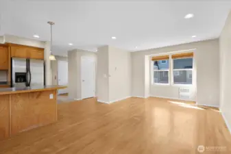 Open-concept space with wood flooring, kitchen cabinetry, stainless steel appliances, and large windows with blinds.