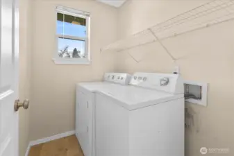 Laundry room with washer and dryer, wall-mounted wire shelf, and window providing natural light.