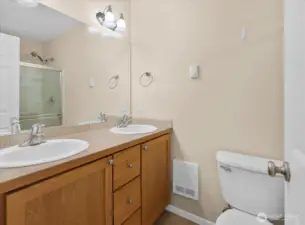Primary bathroom with double-sink vanity, wall mirror, glass-enclosed shower, and toilet.