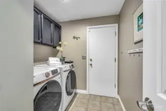 A dedicated laundry room off the garage features brand-new washer and dryer, upper cabinetry for convenient storage, and durable vinyl flooring—offering a clean, organized, and efficient space for handling household tasks.