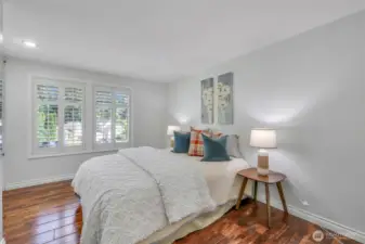 A sunlit upstairs bedroom with plantation shutters and rich-toned flooring offers a peaceful ambiance, ideal for guests or a quiet home office.