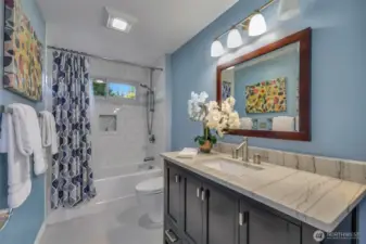 The upstairs hall bath has been stylishly updated with a quartz-topped vanity, subway tile tub surround, and a framed mirror, providing a fresh and functional space for daily routines.