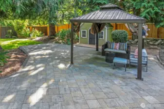 Tucked beneath the shade of towering evergreens, the paved patio offers a cool and calming retreat—ideal for casual lounging, dining, or conversation.