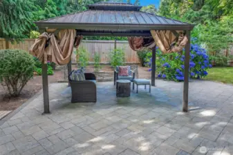Enjoy gatherings in this inviting outdoor lounge space under a metal-roofed gazebo, with views of lush hydrangeas and garden beds all around.
