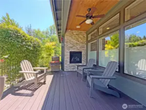 Covered rear deck with ceiling fan, gas fireplace, and view of private gardens.