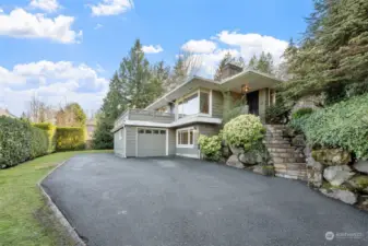 A welcoming entryway with lush landscaping and a beautifully crafted rockery frame the entrance of this charming home. The tiered stone pathway leads to a welcoming front porch surrounded by vibrant greenery.