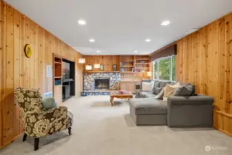 The inviting family room showcases a beautiful stone gas fireplace, built-in shelving, and rich wood paneling for a warm ambiance. Recessed lighting and a large window enhances the room.