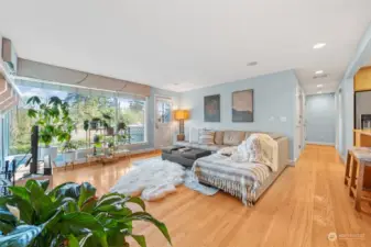 Large windows bring in natural light and offer scenic views of the surrounding greenery. The open layout seamlessly connects the living area to the outdoor deck for easy indoor-outdoor living.