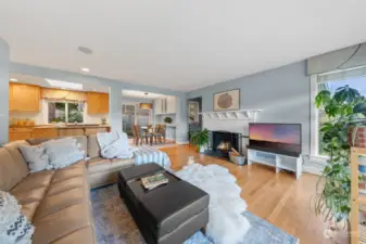 The inviting living room showcases a wood-burning fireplace with a chic mantel, rich hardwood floors, and a seamless flow to the kitchen, dining area, and entryway. Its open layout creates a warm and connected space for both relaxing and entertaining.