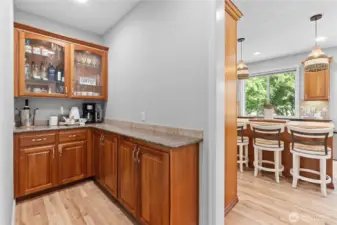 The butler's pantry has granite countertops and rich cherry wood cabinets, including upper glass-front cabinets that add a elegant touch. The wood flooring complements the cabinetry, creating a cohesive and inviting space.