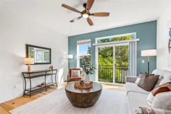 Bask in south-facing sunshine and breezes from the Juliet balcony, with views of trees and the patio below. A smoky blue accent wall and modern ceiling fan set the mood, while the sleek wood-and-concrete staircase anchors the space with architectural flair—making this living room as stylish as it is inviting.