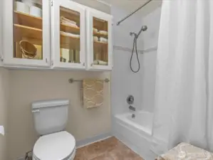 Full bathroom toilet and tub / shower.  The glass doored cabinet with a mirrored back is elegant and useful bathroom storage.