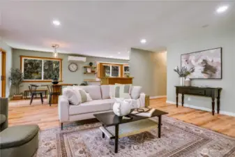 Open-concept layout connects living, dining, and kitchen areas with seamless flow, wood flooring, and soft forest-inspired tones throughout.