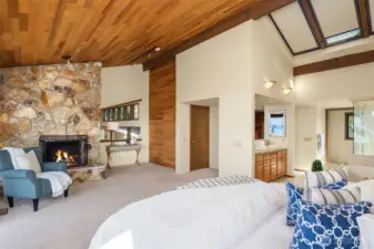 The primary suite features a floor-to-ceiling wood-burning fireplace and a peekaboo opening to the living room below, which could be enclosed for added privacy. The space flows naturally into the adjoining bath.