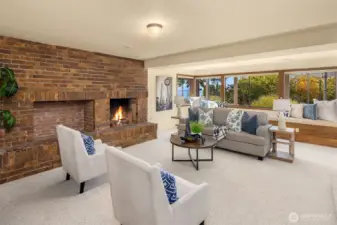 The lower level features a spacious family room with a wood-burning fireplace, built-in bench seating along the wall of windows, and beautiful views.