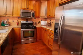 Open kitchen has slab granite countertops, double sink, gas range, extensive strorage, and double-door refrigerator.