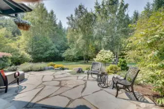 The gorgeous stone patio is an inviting outdoor retreat, perfect for relaxing or entertaining, and seamlessly blends elegance with durability, providing a charming space for dining, lounging, or enjoying the surrounding landscape. Surrounded by lush landscaping and open views of the acreage, this patio creates a serene extension of the home’s indoor living spaces.